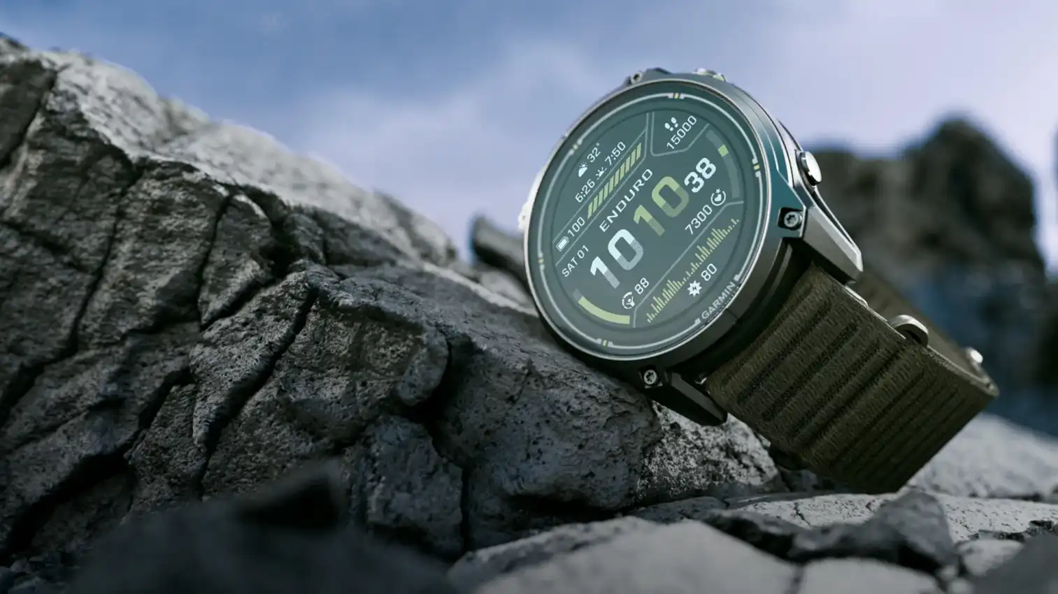 Garmin Enduro 4 titanium sports watch with a dark olive ComfortFit fabric band, resting on rocks