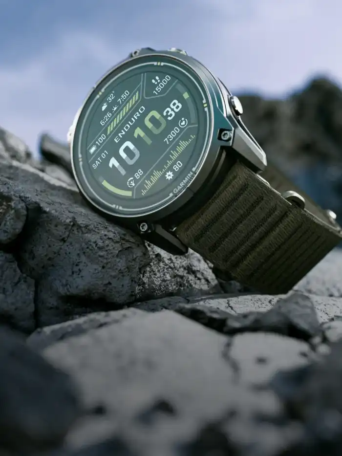 Garmin Enduro 4 titanium sports watch with a dark olive ComfortFit fabric band, resting on rocks